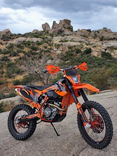 an orange and black dirt bike parked on top of a gravel road next to rocks