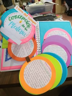 a person holding up some colorful paper discs with writing on them and an open book in the background