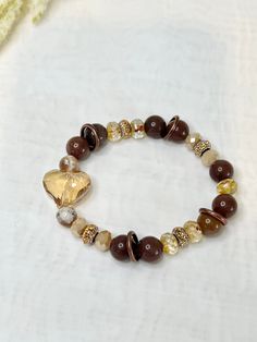 Our New Bonbon Bracelet is a stunning single bracelet with lots of eye catching details. From the ambient  toasted heart as the centerpiece, to the 10mm Creamy chocolate quartz beads. Perfect for fall and winter cozy date nights to casual days in the earthy brown is comforting. Affordable Brown Jewelry With Gold Beads, Cheap Brown Stretch Bracelet For Gift, Elegant Luxury Brown Beads, Luxury Brown Beaded Bracelets With Gemstone, Brown Accessories Aesthetic, Brown Bracelet Aesthetic, Bohemian Heart Bracelet With Colorful Round Beads, Bohemian Crystal Bracelet With Heart Beads, Bohemian Heart Bracelet With Colorful Beads