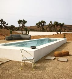 an empty swimming pool in the middle of a desert area with chairs and tables around it