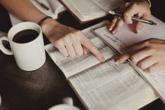 two people are sitting at a table with books and papers, one person is holding a pen