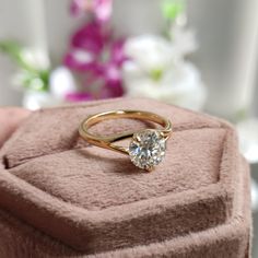 a close up of a person holding a ring on a box with flowers in the background