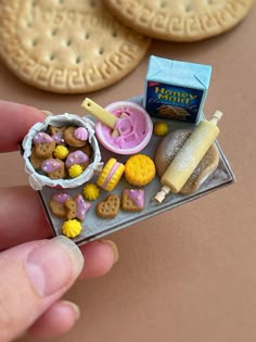 a hand is holding a miniature food tray with cookies, candy and crackers on it