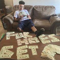 a young man sitting on a couch with stacks of money in front of him,