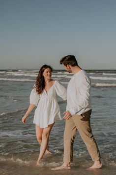 a man and woman are walking in the water at the beach holding each other's hands