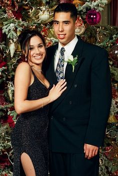 a man and woman standing next to each other in front of a christmas themed wall