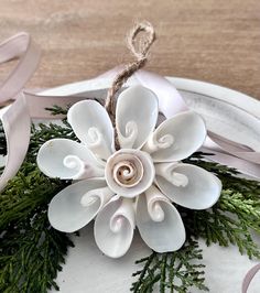 an ornament made out of white flowers and greenery on a plate with ribbon