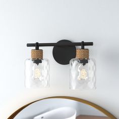 two glass jars are hanging on the wall above a mirror, and one light is turned on