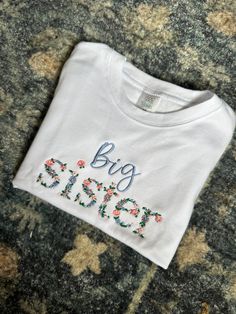 Embroidered floral big sister shirt.  Perfect for a pregnancy announcement! Big Sister Floral Embroidered Shirt - Sibling Pregnancy Announcement - Floral Big Sis Shirt - Floral Big Sister Shirt No returns due to personalization of shirt.  Wash inside out, air dry is possible.  Name under floral "big sis" will be in light blue.  Big Sister Floral Embroidered Shirt - Sibling Pregnancy Announcement - Floral Big Sis Shirt - Floral Big Sister Shirt Floral Embroidered Shirt, Pregnancy Announcement Sibling, Big Sister Announcement, Embroidery Letters, Big Sis, Big Sister Shirt, Sister Shirts, Shirt Embroidery, Big Sister