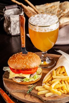 a hamburger and fries on a wooden plate with a glass of beer next to it