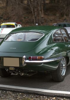 an old green car is parked on the side of the road in front of other cars