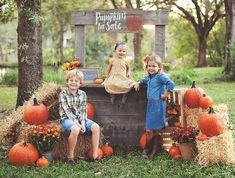 two children sitting on top of a wooden crate with pumpkins and hay bales