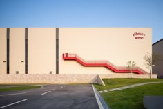 an empty parking lot in front of a large building with a red staircase going up the side