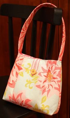 a purse sitting on top of a wooden chair next to a black chair with a white and pink flowered bag