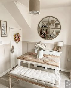 a white bench sitting under a round mirror next to a table with flowers on it