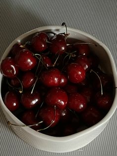 a white bowl filled with lots of cherries on top of a gray tablecloth