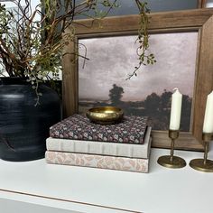 two candles are sitting on top of some books next to a vase with branches in it