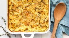 a casserole dish with potatoes and herbs in it next to a wooden spoon