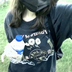 a woman wearing a face mask and holding a water bottle in her hand while standing on the grass