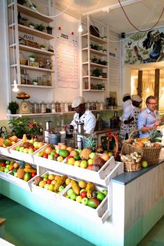 several people in a kitchen preparing food for customers to eat at the counter and behind them are shelves filled with fruit