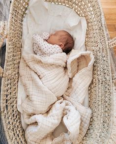 a baby wrapped in a blanket is laying in a wicker basket on the floor