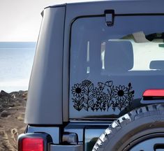 a jeep parked on the beach with flowers painted on it's rear window and side door