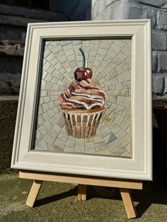 a cupcake with icing and a cherry on top is displayed in a white frame