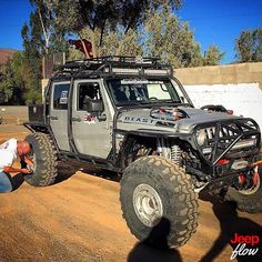 a man is working on a jeep in the dirt with another man looking at it