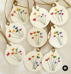 six tags with flowers painted on them hanging from twine