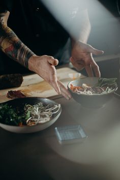 a person reaching for food in a bowl on a table with other dishes and utensils