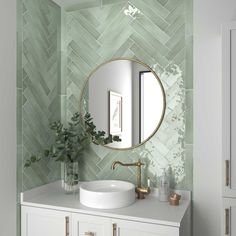 a bathroom with green tiles and a round mirror on the wall above the sink, along with a plant in a vase