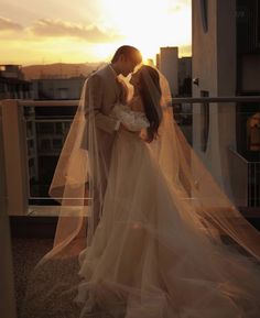 a bride and groom kissing in front of the sun setting on top of a building