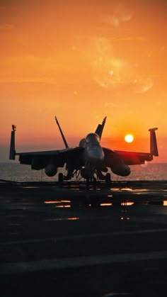 a fighter jet sitting on top of an airport tarmac at sunset with the sun in the background