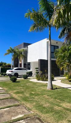 a white car is parked in front of a modern house with palm trees and landscaping