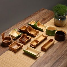 a wooden table topped with lots of different types of bowls and trays next to a potted plant