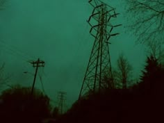 an electric pole in the dark with power lines and trees behind it on a gloomy day