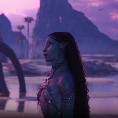 a woman with long hair standing in front of mountains and palm trees at sunset or dawn