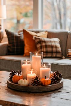 candles are arranged on a tray with pine cones and pumpkins in front of the window