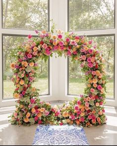 a flowered arch with pink and orange flowers in front of a large open window