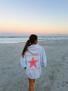 a girl walking on the beach wearing a hoodie that says look forward to the future