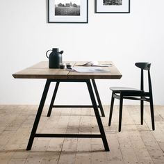 two framed pictures hang on the wall above a wooden table with chairs and a coffee pot