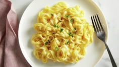 a white plate topped with pasta and parsley on top of a pink napkin next to a fork