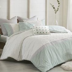 a bed with white and blue comforters in a room next to a window on the floor