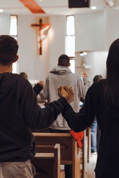 two people holding hands while standing in front of pews with other people behind them