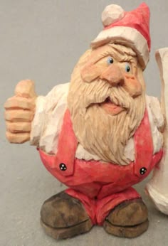 a ceramic figurine of a santa clause holding a piece of paper and giving the thumbs up