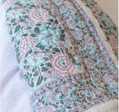 a close up of a pillow on a bed with white sheets and pink, blue and green flowers