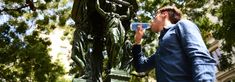 a man standing next to a statue holding a toothbrush in his hand and looking at it