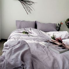 an unmade bed with purple sheets and flowers on the headboard in front of it