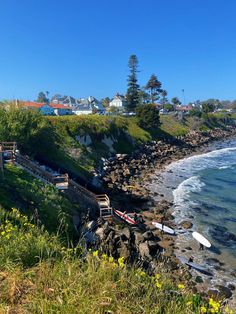 a view of the ocean and shore with houses in the background, along with surfboards laying on the rocks