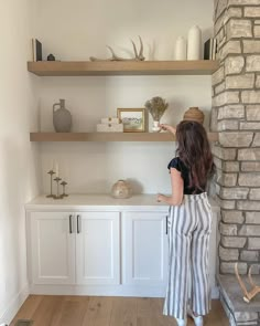 a woman standing in front of a shelf with vases and other items on it